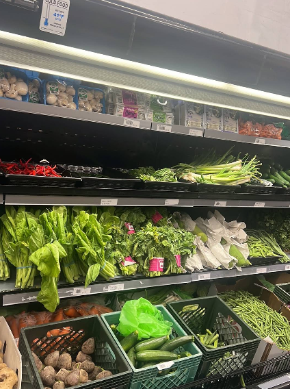 Grocery store produce aisle with refrigerated shelves of fresh leafy greens, mushrooms and vegetables